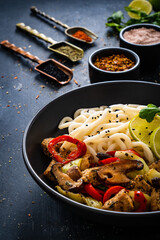 Chicken nuggets with noodles and stir fried vegetables on black table

