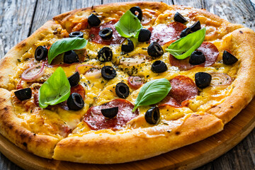 Circle pepperoni pizza with mozzarella cheese and black olives on wooden table

