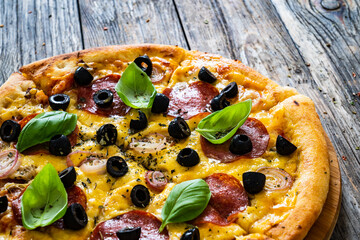 Circle pepperoni pizza with mozzarella cheese and black olives on wooden table
