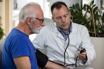 Doctor examining senior male patient by measuring blood pressure at home. Elderly people medicare, healthcare, hypertension concept