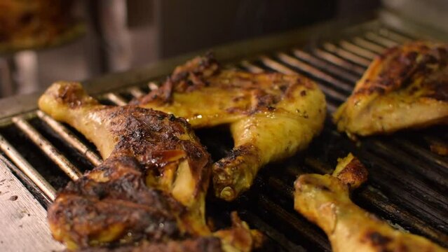 Close-up of grilled juicy chicken legs on the grill BBQ. Golden crispy skin chicken meat with spices on grid. Side view from above