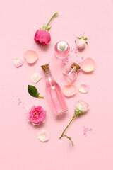 Bottles of cosmetic oil with rose extract and flowers on pink background