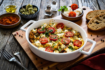 Bread casserole with feta cheese, tomatoes and eggs on wooden table
