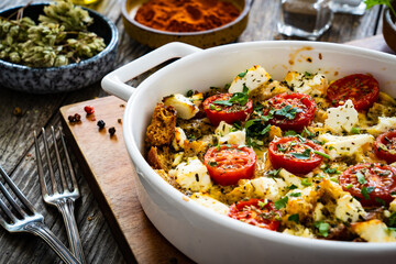 Bread casserole with feta cheese, tomatoes and eggs on wooden table

