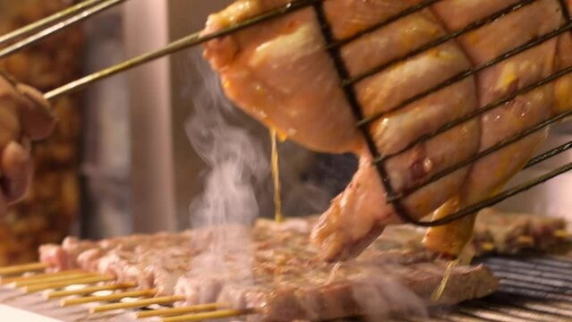 Close-up of hands turns the grilled chicken over the gril BBQ. Flattened out barbecued golden crispy skin chicken tabaka on grid. Whole juicy with spices grilled chicken tabaka. Selective focus