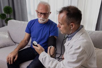 Doctor examining senior male patient by measuring blood pressure at home. Elderly people medicare, healthcare, hypertension concept