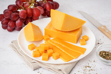 Plate with tasty cheddar cheese on light background