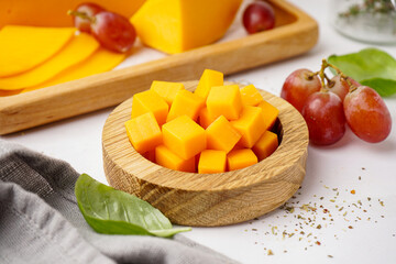 Bowl with pieces of tasty cheddar cheese on light background