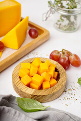 Bowl with pieces of tasty cheddar cheese on light background