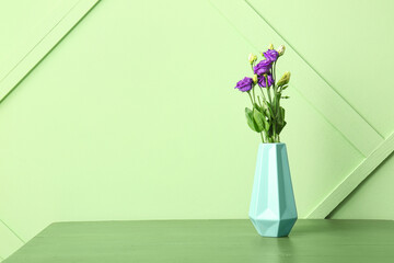 Vase with eustoma flowers on table near green wall