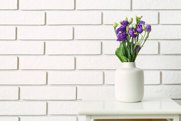 Vase with eustoma flowers on table near white brick wall