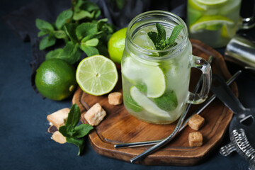 Mason jar of cold mojito and ingredients on dark background