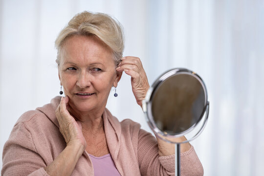 Senior woman looking at her reflection in the mirror and smiling happy with appearance. Aging and beauty concept