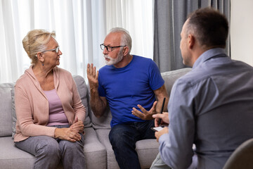 Unhappy senior couple arguing, having fight, disagreement at psychologists office. Frustrated elderly wife and husband discussing relationship problems with their therapist