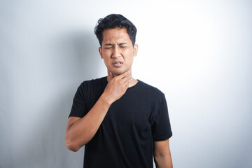 Young Asian man having sore throat and touching his neck, wearing a loose black t-shirt against white background. Hard to swallow