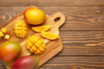 Cutting board with fresh ripe mangoes on wooden background