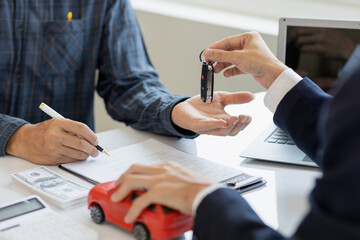The young businessman made a lease for a new car in the office of a car dealer and received the keys after the contract was completed. The concept of a car purchase contract - obrazy, fototapety, plakaty