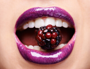 Closeup of woman lips with purple lipstick, makeup and beauty with shine and vibrant aesthetic, creativity and glow. Fruit between female model teeth, cosmetic product for mouth and cosmetology