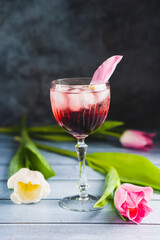 Pink cocktail with champagne or prosecco and ice in crystal wine glass and white and white tulips