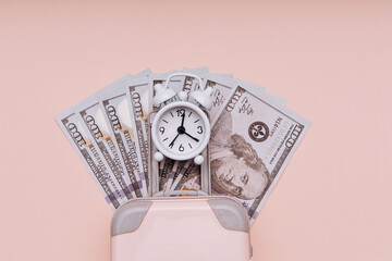 Travel luggage with alarm clock and dollar banknotes. Savings and travelling. Close-up