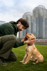 A brunette sits on the grass outside and pets her dog. A bearded man pets his spaniel dog while walking in the park.