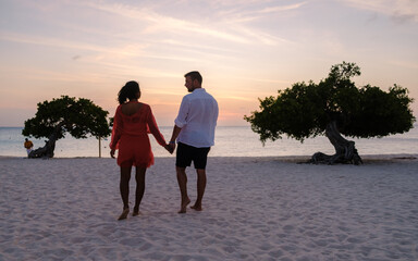 Divi Divi Trees on the shoreline of Eagle Beach in Aruba, a couple of men, and a woman on the beach of Aruba during sunset