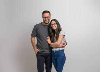 Fototapeta premium Portrait of affectionate young girlfriend and boyfriend holding hands and standing happily against background. Cheerful couple wearing eyeglasses embracing and looking at camera
