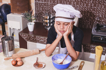 Cute Asian little kid in chef uniform rest his chin on his hands is bored of cooking, feeling tired and dissapointed. 