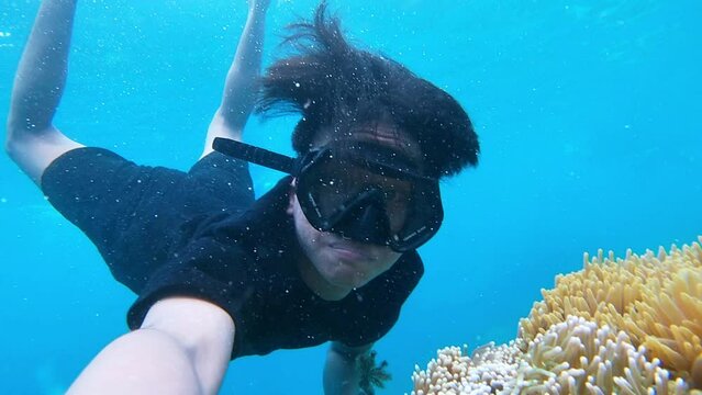 an underwater footage of asian man snorkeling in the sea using snorkel mask  showing nemo fish and anemon