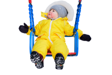 Toddler baby boy in a yellow snowsuit is swinging on a swing in a snowy playground, isolated on white background. Child age one year five months playing on a winter walk