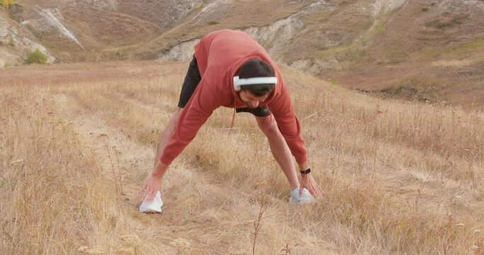 handsome Caucasian man wearing headphones stretches his hamstrings. athletic man exercising outdoors. male athlete warm up for wellness, exercise and balance