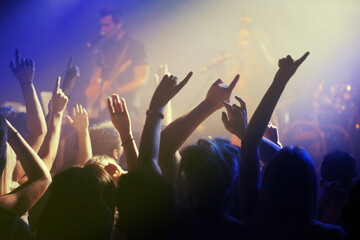 Hands in air, people dancing at concert or music festival with neon lights and energy at live event. Dance, fun and excited crowd of fans in arena for rock band, musician performance and spotlight.