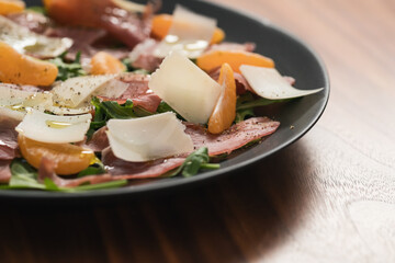 Salad with prosciutto, tangerines and vintage cheese on walnut table