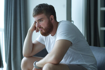 Depressed unhappy middle-aged sad man sitting on couch in living room, leaning on his hands, having troubles loneliness, home interior, holding his forehead while having a headache