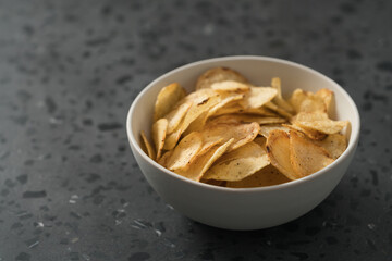 Organic potato chips with black pepper in white ceramic bowl on concrete background with copy space