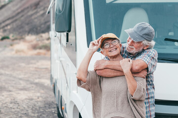 Happy senior couple on leisure trip enjoying travel destination standing outside a camper van...