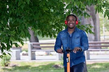 Cute black student enjoys nature riding an electric scooter in a large green park on a sunny day....