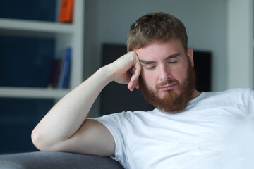 Portrait young european beard pensive thoughtful relaxed lonely guy, man is dreaming, thinking, relax at home in living room at comfortable sofa, couch with his hands behind head 