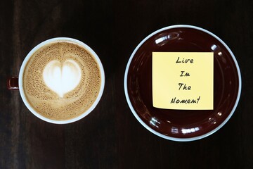 Coffee cup and handwritten note note LIVE IN THE MOMENT, concept of live with the present - be with...