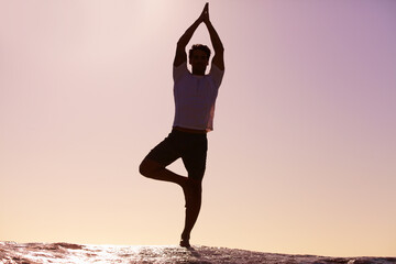 Man, silhouette and yoga in sunset meditation on beach for spiritual wellness, inner peace or mental wellbeing in nature. Male yogi in tree pose for balance, healthy body or mindfulness on ocean rock