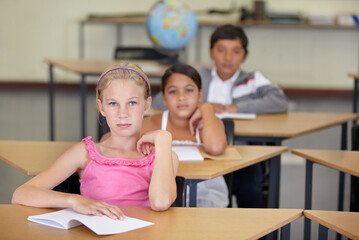 Portrait, serious kids and student in classroom with book, ready to learn and study in class. Group of students, education and girl learning in primary school for knowledge, development or studying.