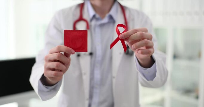 Doctor in white lab coat holds red ribbon and condom in hands. International symbol of AIDS and HIV awareness and health protection slow motion