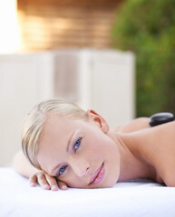 Face of woman, hot stone massage at spa with healing and wellness, holistic treatment at luxury resort. Stress relief, zen and female person with rocks on back in portrait, self care and therapy