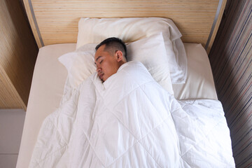 Man wrapped with white soft blanket sleeping in bed at home