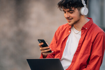 young man or student with mobile phone laptop and headphones in the street