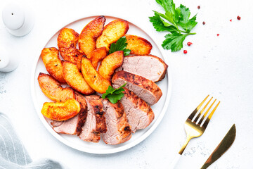 Baked pork tenderloin and quince or apple slices with parsley served on white plate. White table background, top view