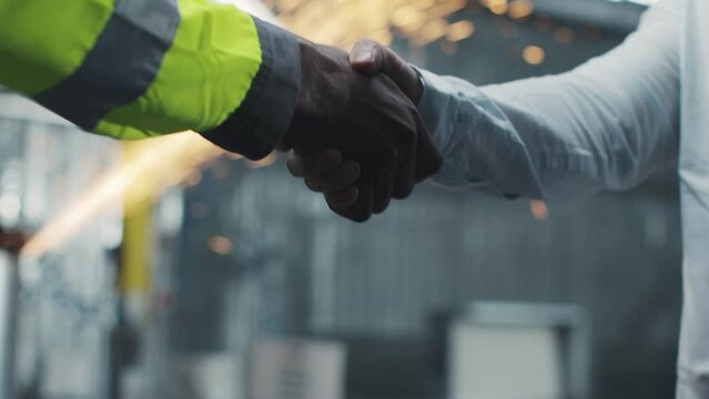 Two multicultural men shaking hands at manufacturing factory. Cooperation of workers on unfocused background with welding sparks flying. Two businessmen making deal. Ethnic diversity.