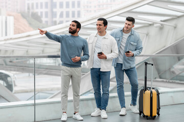 Fototapeta premium Three Tourists Men Using Phones Pointing Finger Aside At Airport