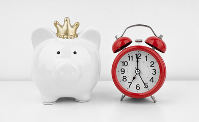 Red alarm clock with piggy bank against a white wall. Financial concept.