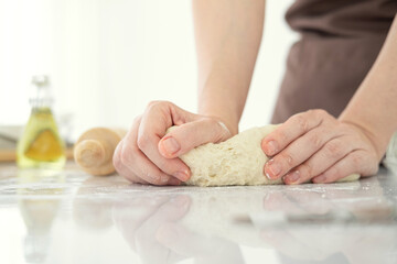 Woman hands kneading dough on table, closeup. Woman kneading dough on table sprinkled with flour.Making bakery by female hands in bright light kitchen at home.
